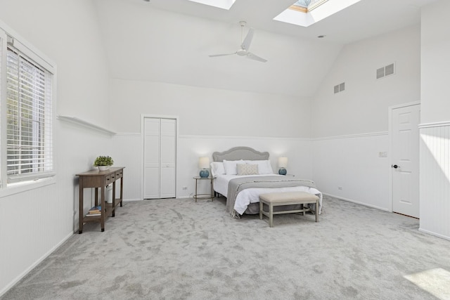 carpeted bedroom featuring a skylight, visible vents, high vaulted ceiling, and a wainscoted wall
