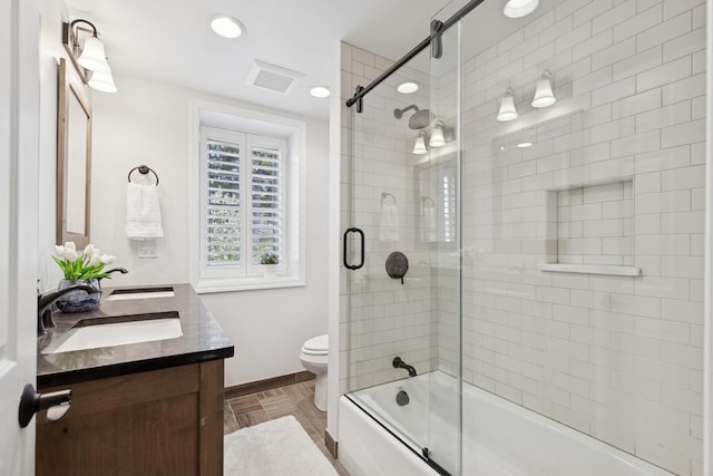 bathroom featuring a sink, combined bath / shower with glass door, toilet, and double vanity