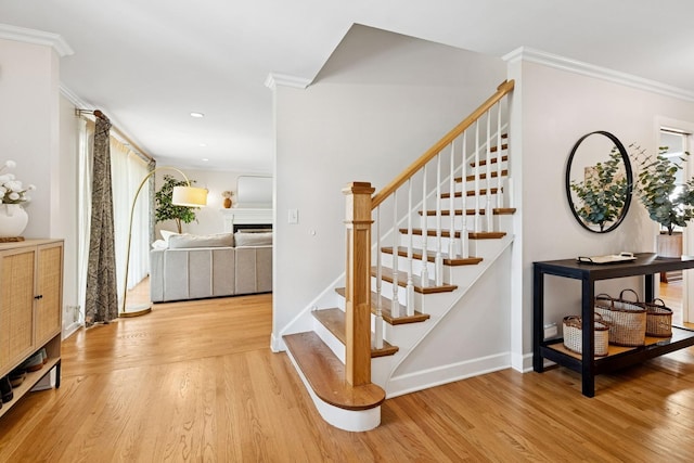 stairs with baseboards, ornamental molding, a fireplace, and wood finished floors