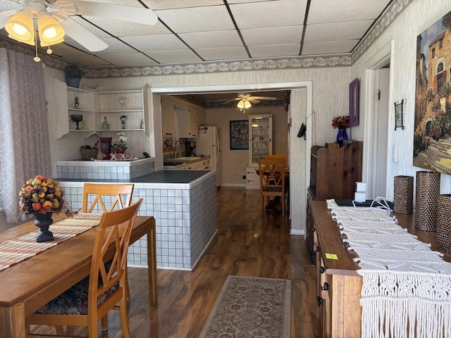 dining area with ceiling fan, dark wood finished floors, a paneled ceiling, baseboards, and wallpapered walls