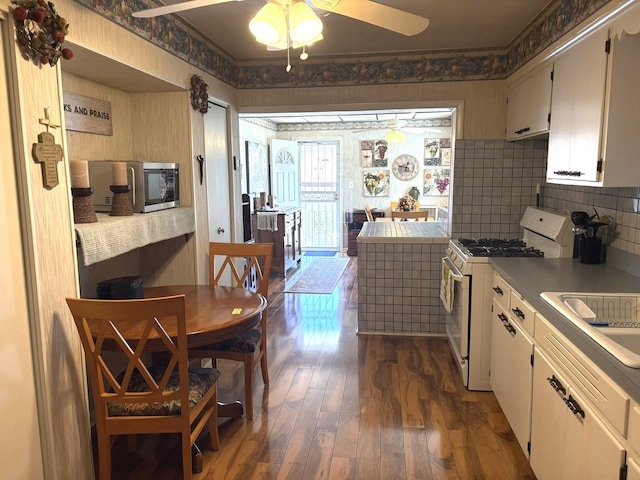 kitchen with dark wood-style flooring, a ceiling fan, stainless steel microwave, backsplash, and white range with gas cooktop