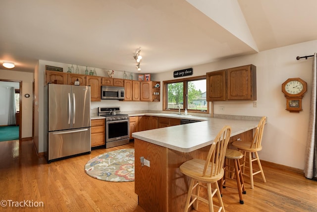 2803 Monterra Dr, Spring Grove, IL 60081 - kitchen featuring stainless steel appliances, a peninsula, light wood-style flooring, light countertops, and brown cabinetry
