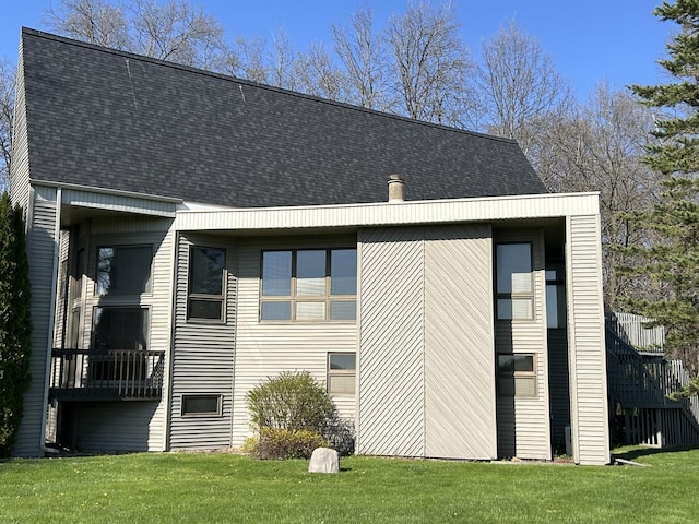 rear view of property featuring a shingled roof and a lawn