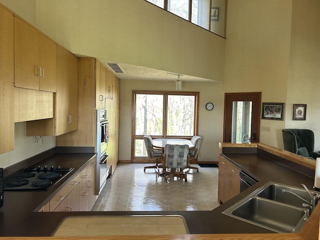 kitchen with a high ceiling, a sink, black appliances, visible vents, and dark countertops