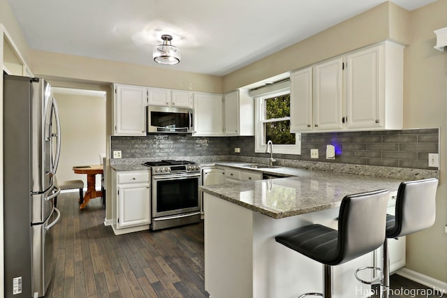kitchen featuring stainless steel appliances, a peninsula, a sink, light stone counters, and white cabinets
