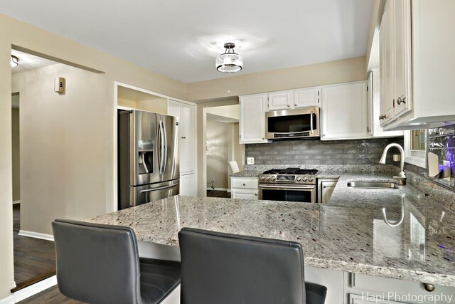 kitchen featuring stainless steel appliances, a sink, a peninsula, tasteful backsplash, and light stone countertops