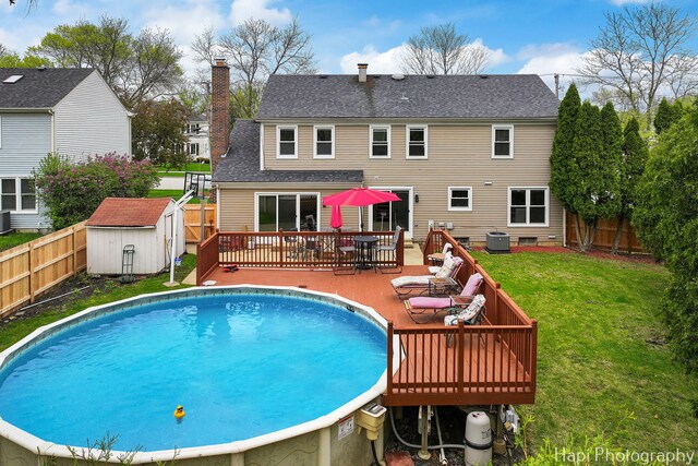 view of pool with a wooden deck, a shed, central AC, and an outdoor structure