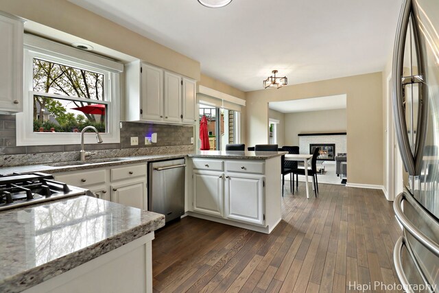 kitchen with appliances with stainless steel finishes, a sink, a peninsula, white cabinetry, and backsplash