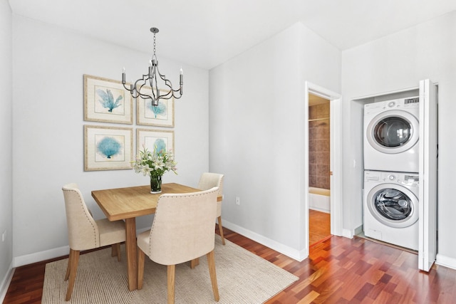 dining area featuring stacked washer and dryer, a notable chandelier, dark wood-style flooring, and baseboards