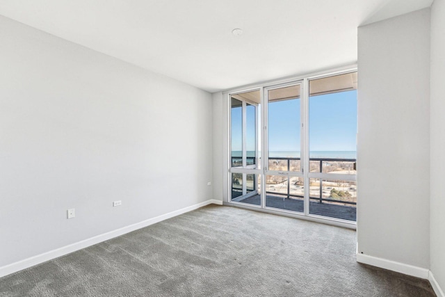 carpeted empty room with baseboards, a water view, and expansive windows