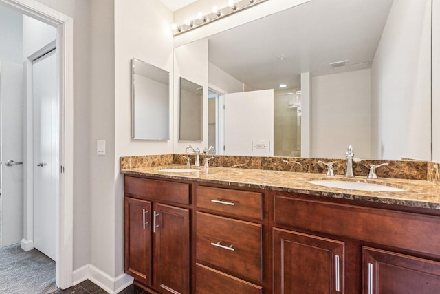 full bath with a shower with shower door, double vanity, a sink, and baseboards