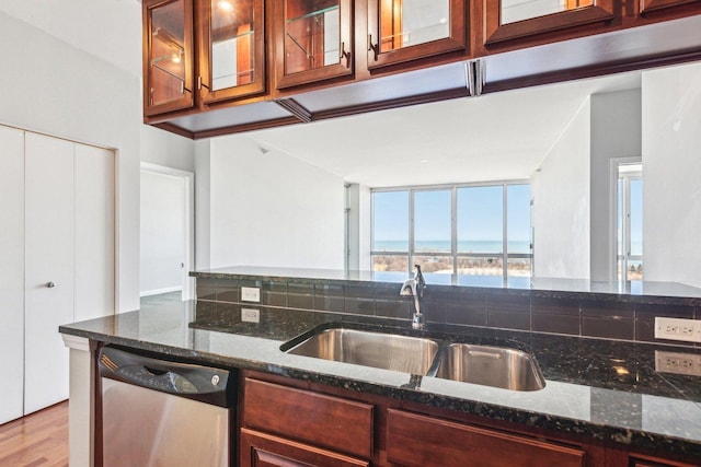 kitchen with dark stone countertops, stainless steel dishwasher, glass insert cabinets, a sink, and a water view