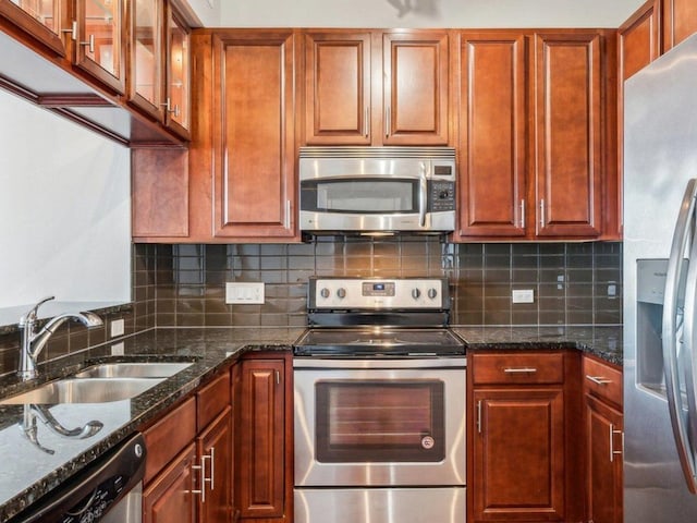 kitchen featuring dark stone counters, stainless steel appliances, decorative backsplash, and a sink