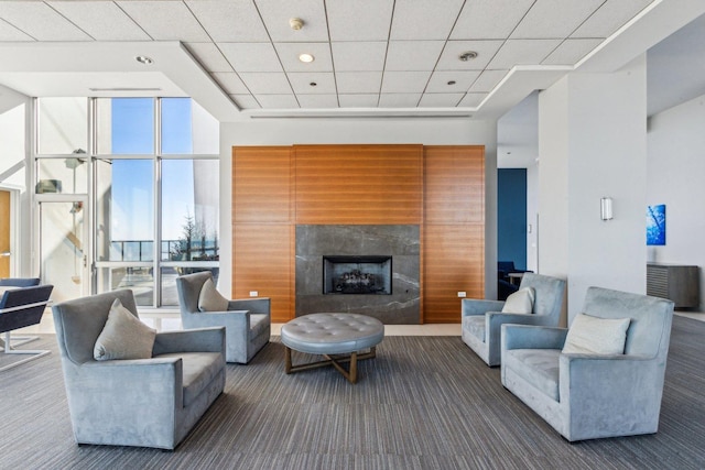 living area with a tile fireplace, a paneled ceiling, expansive windows, and carpet