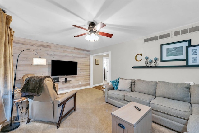 living room featuring light colored carpet, visible vents, wooden walls, a ceiling fan, and baseboards