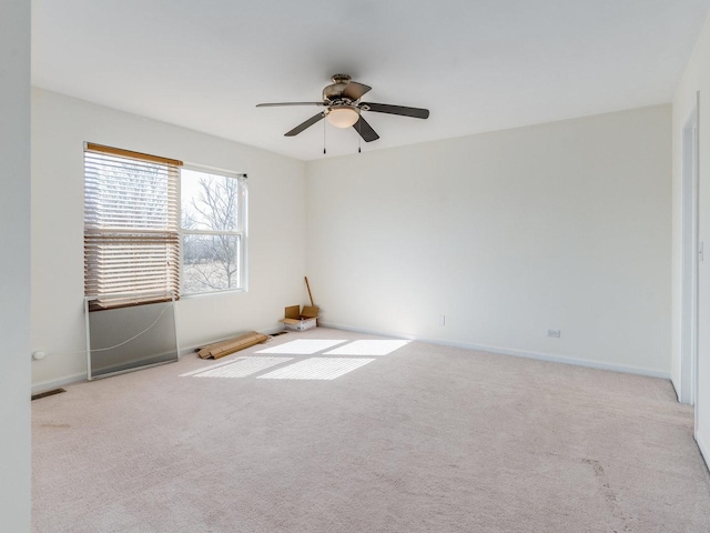 carpeted spare room with a ceiling fan and baseboards