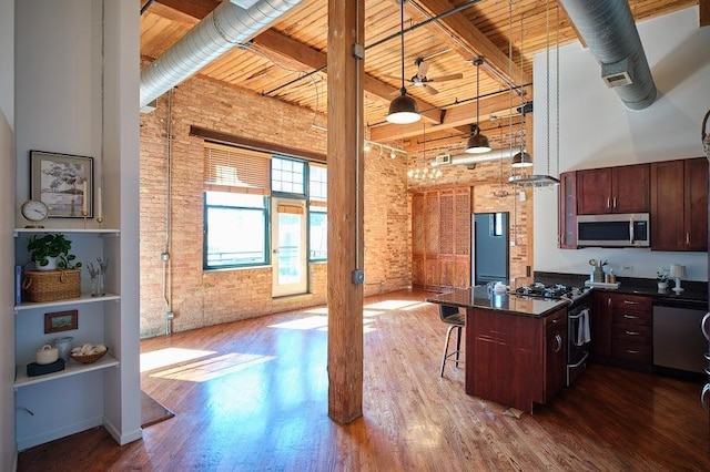 kitchen with brick wall, dark countertops, appliances with stainless steel finishes, wooden ceiling, and a high ceiling