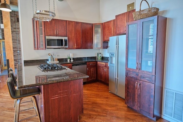 kitchen featuring dark wood-style flooring, visible vents, appliances with stainless steel finishes, a peninsula, and glass insert cabinets