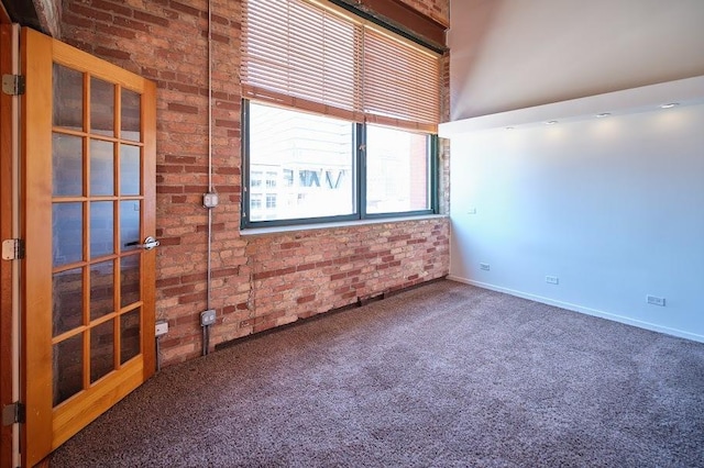 empty room featuring carpet floors, baseboards, and brick wall