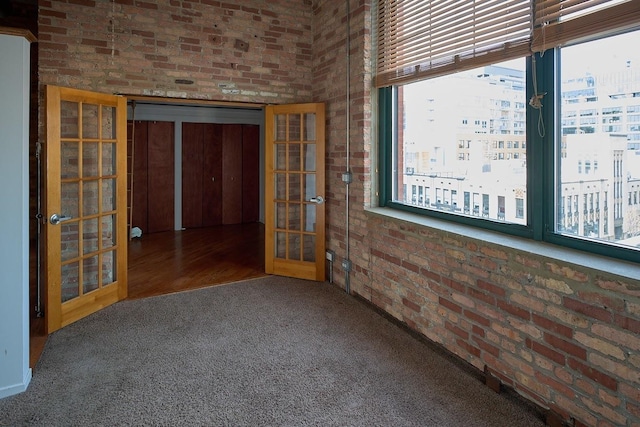 carpeted spare room with brick wall and french doors