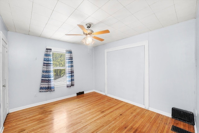 spare room featuring wood finished floors, ceiling fan, visible vents, and baseboards
