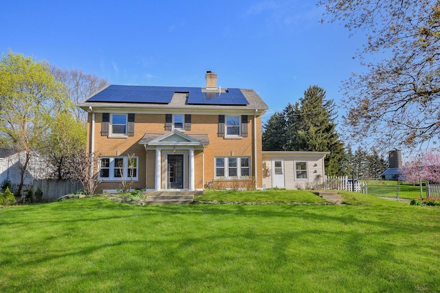 back of house featuring a yard, fence, a chimney, and solar panels
