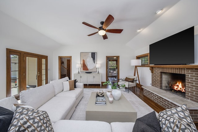 living room with a ceiling fan, wood finished floors, vaulted ceiling, and a fireplace
