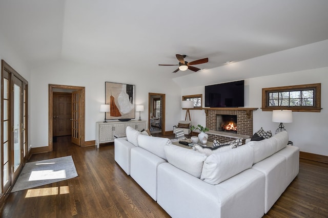 living room with a ceiling fan, dark wood-style flooring, a fireplace, vaulted ceiling, and baseboards