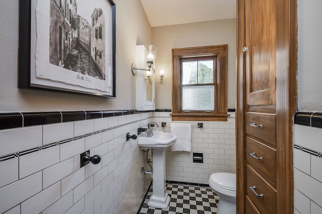 half bath featuring tile walls, tile patterned flooring, a sink, a wainscoted wall, and toilet