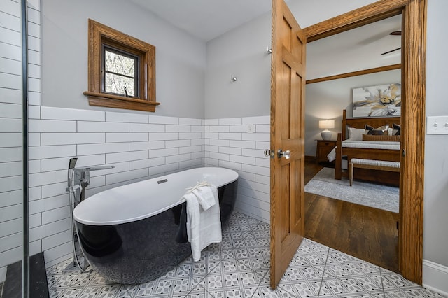 full bathroom with ensuite bathroom, wainscoting, a soaking tub, and tile walls