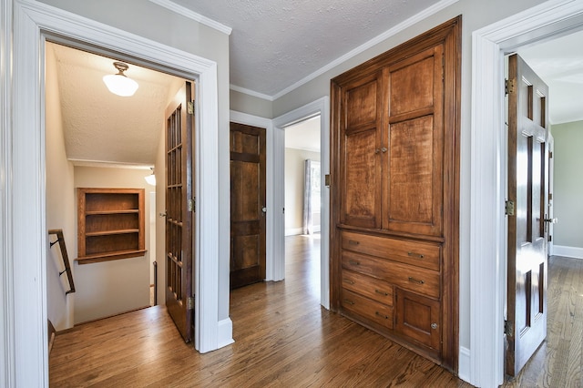 hallway with a textured ceiling, dark wood finished floors, ornamental molding, and baseboards