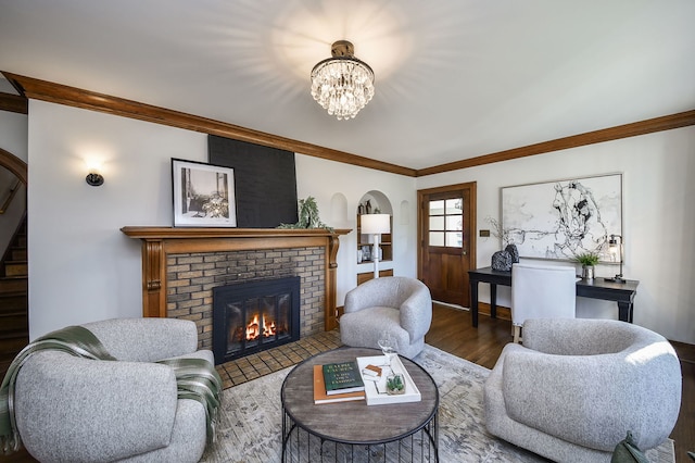 living area featuring arched walkways, a fireplace, wood finished floors, a chandelier, and ornamental molding