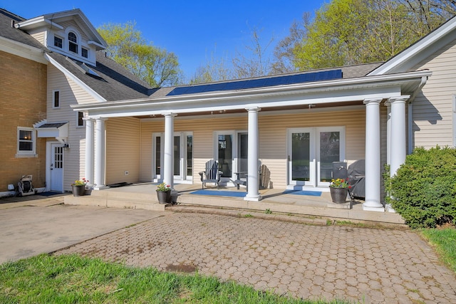 rear view of house with a porch, a shingled roof, and french doors