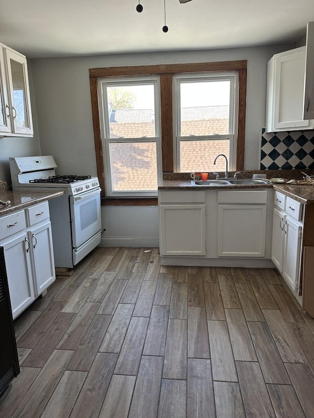kitchen featuring tasteful backsplash, white cabinets, a sink, white range with gas cooktop, and wood finished floors