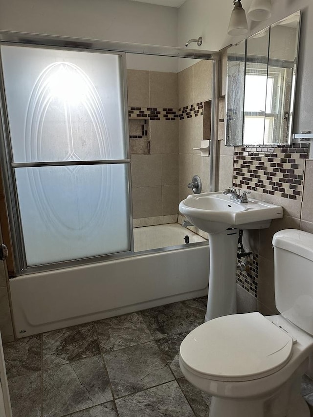 bathroom with combined bath / shower with glass door, toilet, tasteful backsplash, and tile walls