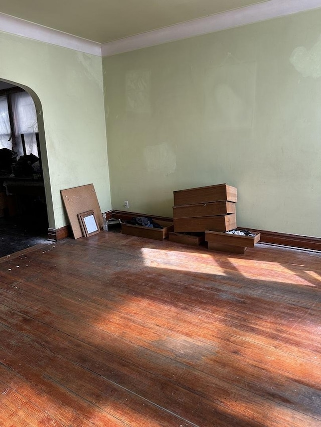 unfurnished living room featuring baseboards, arched walkways, crown molding, and wood-type flooring