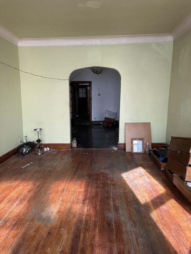 spare room featuring wood-type flooring, arched walkways, and baseboards