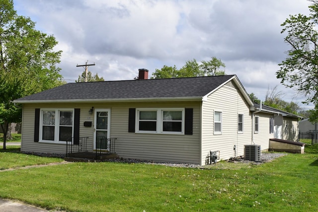 view of front of house featuring a front lawn, a chimney, and central AC
