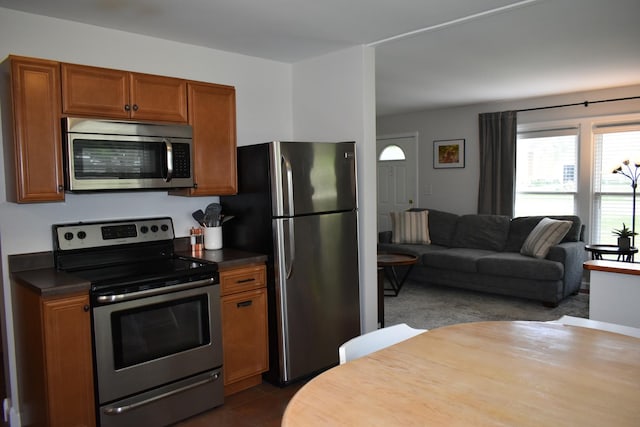 kitchen featuring brown cabinets, dark countertops, dark tile patterned flooring, open floor plan, and appliances with stainless steel finishes