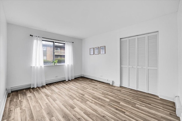 unfurnished bedroom with baseboard heating, light wood-type flooring, a closet, and baseboards