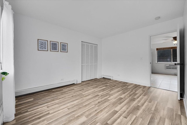 unfurnished bedroom with an AC wall unit, a closet, wood finished floors, and a baseboard radiator