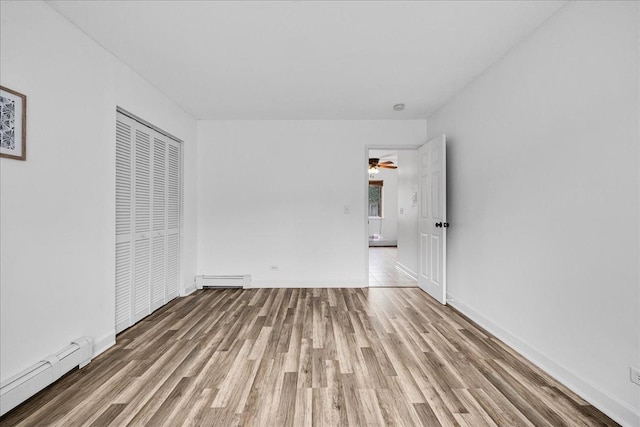 unfurnished bedroom featuring wood finished floors, a baseboard radiator, a closet, baseboard heating, and baseboards