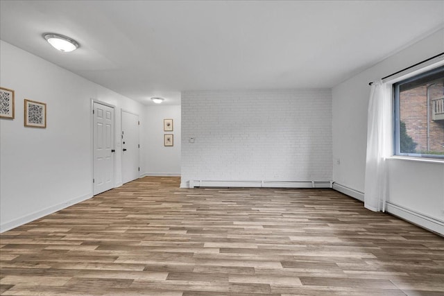 spare room with baseboards, baseboard heating, wood finished floors, and brick wall