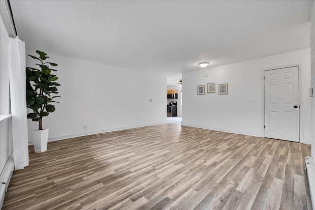 unfurnished living room featuring a baseboard heating unit, ceiling fan, baseboards, and light wood-style floors
