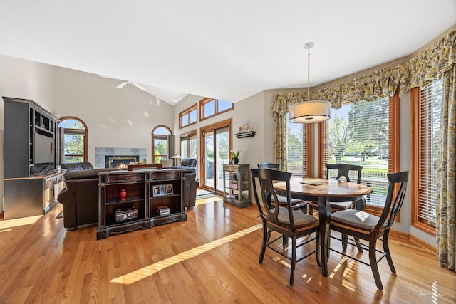 dining area featuring healthy amount of natural light, a ceiling fan, light wood-type flooring, a warm lit fireplace, and vaulted ceiling