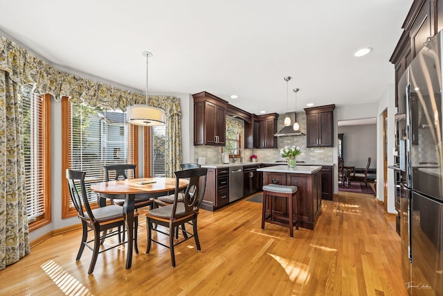 kitchen featuring wall chimney exhaust hood, appliances with stainless steel finishes, a center island, dark brown cabinetry, and light countertops