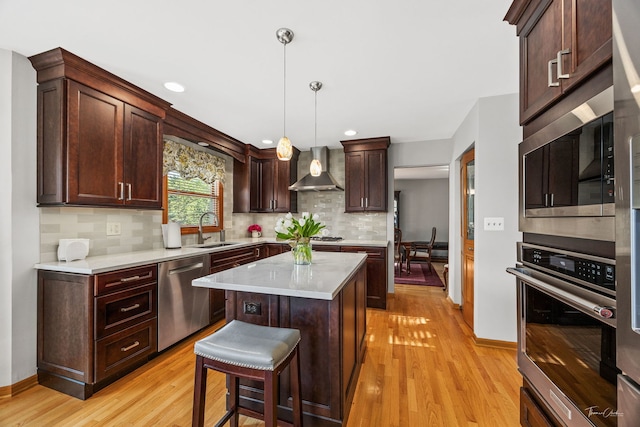 kitchen featuring appliances with stainless steel finishes, wall chimney exhaust hood, a sink, tasteful backsplash, and light wood-type flooring