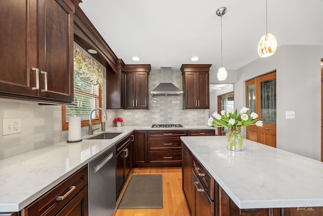 kitchen with wall chimney exhaust hood, a sink, light wood finished floors, stainless steel appliances, and light stone countertops