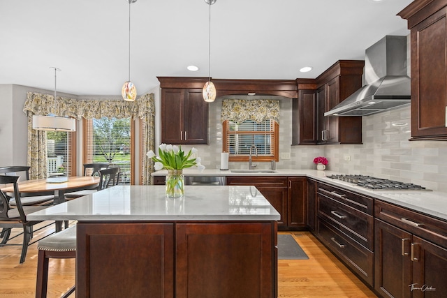 kitchen featuring wall chimney range hood, a sink, light wood-style floors, backsplash, and a kitchen island