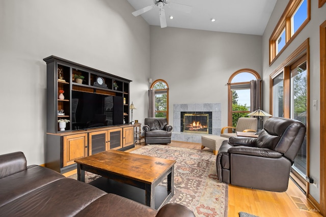 living area with a towering ceiling, ceiling fan, light wood-type flooring, a premium fireplace, and recessed lighting